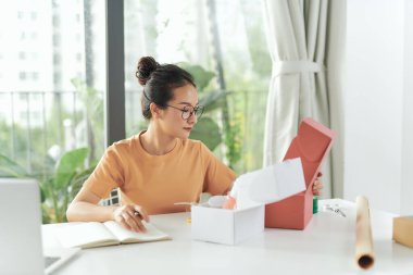 Kadın, çevrimiçi dükkanının ürününü müşteriye göndermek için paketliyor..