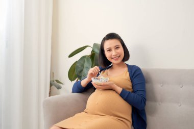 Kanepede sütlü ve sağlıklı kahvaltılı genç Asyalı hamile kadın.
