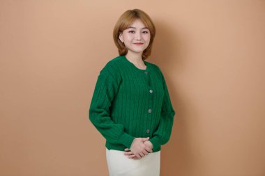 Güzel, çekici bir gülümseme portresi. Olumlu pozlarda genç, Asyalı bir kadın bej arka planda mutlu bir şekilde kameraya bakıyor..