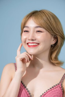 Yakın plan rüya gibi, yaratıcı Asyalı kadın yaz tatilini hayal ediyor, mükemmel bir tatil hayal ediyor, düşünceli, dokunaklı yanaklı, yukarı bakıyor, mavi arka planda duruyor.