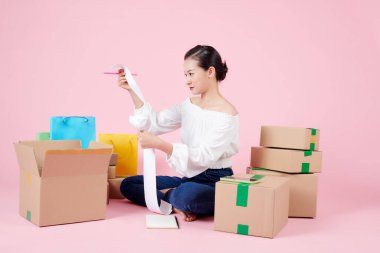 Genç bir Asyalı kadın satış makbuzunu ve paket kutusunu kontrol ederek müşterilere mal teslim etmeye hazırlanıyor. 