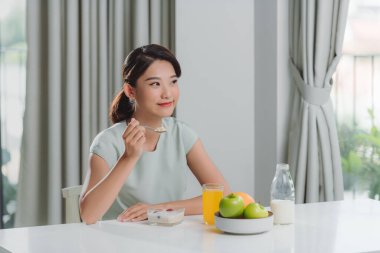 asian young woman having cereals, granola with fresh dairy milk in bowl in kitchen.