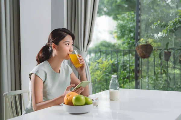 Woman Having Orange Juice While Using Mobile Phone Home — Fotografia de Stock