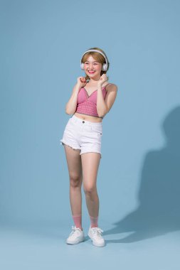 Upbeat positive Asian girl enjoys every bit of music wears stereo headphones on her ears , listens to favorite audio track