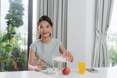 Female hand holding glass bottle pouring milk in cereal granola flakes bowl 