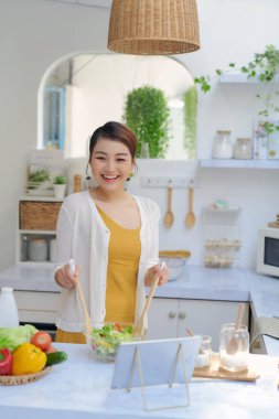 Young woman watching recipe in digital tablet while cooking lunch in the kitchen