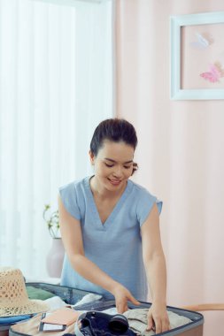 Mutlu kadın yeni bir yolculuk için renkli yaz kıyafetlerini bavula koyuyor.