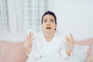 Sick Asian woman using  tissues to sneeze and blowing her nose in winter at home. Her getting sick with flu and cold.