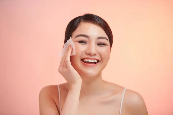 Smiling woman using facial oil blotting paper portrait.