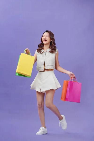 年轻女人开心的笑着去散步抱着购物袋卖紫色背景的东西 — 图库照片