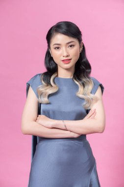 Asyalı, güzel, modaya uygun elbiseli, el ele tutuşmuş, pembe arka plandaki kameraya gülümseyen bir şekilde poz veren genç bir manken..