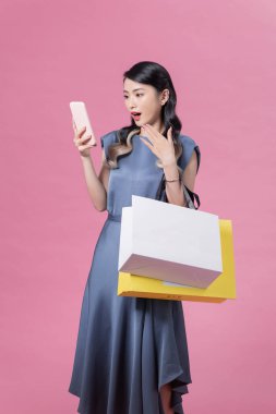 Şok olmuş ve heyecanlı alışveriş kadını pembe izole edilmiş arka planda akıllı telefon uygulaması kullanıyor.