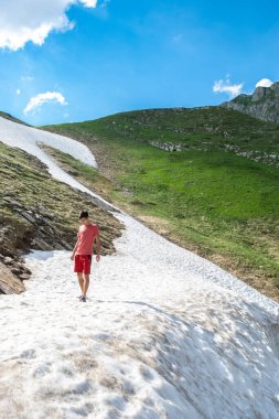 Karadağ 'ın en yüksek karayolu olan yüksek bir dağ yolunun yakınındaki bir dağ yamacında uzanan karda yürüyen turist görülüyor. Durmitor Ulusal Parkı. Yaz güneşli yeşil manzara.