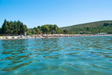 Plavi Horizonti plajı, Karadağ - 28 Haziran 2021: Çam ormanıyla çevrili temiz suyla kumlu plajda tatil yapanlar çocuklar için harika. Yaz güneşli manzarası. Radovici. Tivat Koyu.