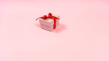 Küçük gri hediye kutusu, kırmızı kurdeleyle bağlanmış ve sevilen kişiye hediye edilmiş, izole edilmiş açık pembe pastel arka plan. Uzayı kopyala Tatil için hediye hazırlama kavramı.