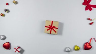 4k Brown hediye kutusu kırmızı kurdeleyle bağlanmış, çerçevede beliriyor, daire çiziyor ve düşüyor. Tatil ve hediye hazırlama kavramı. Açık gri arkaplan. Düz yatıyordu. Uzayı kopyala Hareketi durdur