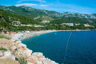 Güneşli bir yaz akşamında mavi gökyüzü arka planında Rafailovici köyü yakınlarındaki yeşil dağlarla çevrili bir körfezdeki Kamenovo çakıl taşı plajının güzel manzarası. Budva Riviera. Karadağ.