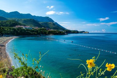 Güneşli bir yaz sabahı, mavi gökyüzü arka planında Rafailovici köyü yakınlarındaki yeşil dağlarla çevrili bir körfezdeki Kamenovo çakıl taşı plajının güzel manzarası. Budva Riviera. Karadağ.