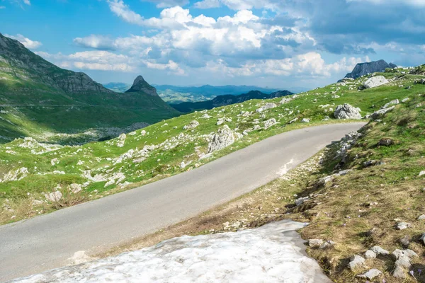 前景には雪のドリフトと風景山の道 モンテネグロで最も高い道路のパス デュルモーター国立公園 夏の日当たりの良い緑の風景 — ストック写真