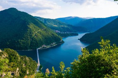 Piva Gölü üzerindeki köprü Pluzine yakınlarındaki yüksek yeşil dağlar arasındaki bir kanyonda yer alıyor. Yaz manzarası. Kuzey Karadağ. Balkanlar 'ın güzel doğası.