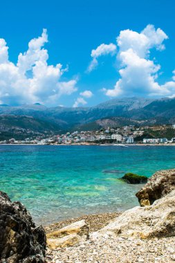 Himare 'nin dağların eteğindeki güzel çakıl taşı plajı. Adriyatik Denizi. Arnavutluk. Yaz bulutu manzarası. Yaz tatili ve rahatlama kavramı