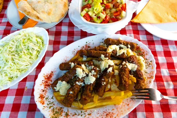 Serbian national dish cevapcici or cevapi (minced meat sausages reminiscent of kebab) along with french fries and salads in the background. The concept of national food.