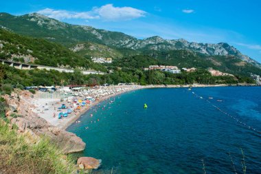 Güneşli bir yaz akşamında mavi gökyüzü arka planında Rafailovici köyü yakınlarındaki yeşil dağlarla çevrili bir körfezdeki Kamenovo çakıl taşı plajının güzel manzarası. Budva Riviera. Karadağ.