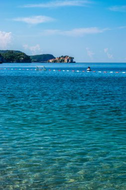 Güneşli yaz sabahında Rafailovici köyü yakınlarındaki bir körfezde Adriyatik Denizi 'nin berrak sularıyla güzel çakıl taşı plajı. Aman Sveti Adası 'nın arka tarafında. Budva Riviera. Karadağ.