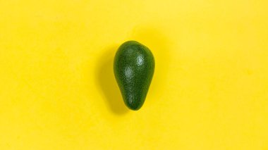 Sarı arka planda yeşil, olgun bir avokado. Düzgün beslenme ve sağlıklı meyve kavramı. Düz yatıyordu.