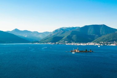 Küçük Our Lady of Mercy (Gospa od milosrda) Adası ve arka planda Tivat kenti ve Vrmac dağı yakınlarındaki Porto Montenegro Marina. Adriyatik Denizi 'nin Kotor Körfezi. Karadağ. Mavi yaz manzarası.