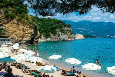 Morgen plajı, Karadağ - 4 Temmuz 2021: Budva yakınlarındaki kumlu plajda güneş pansiyonları ve şemsiyeler. Yaz güneşli manzarası.