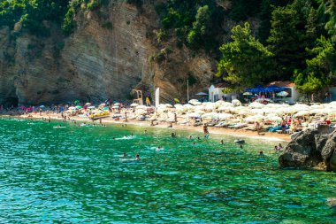 Morgen plajı, Karadağ - 4 Temmuz 2021: Budva yakınlarındaki kumlu plajda güneş pansiyonları ve şemsiyeler. Yaz güneşli manzarası.