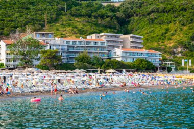 Jaz Beach, Karadağ - 4 Temmuz 2021: Güneşli şezlonglar ve şemsiyelerle kumlu kumsalda dinlenen insanlar. Budva Riviera. Yaz güneşli manzarası.