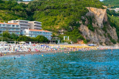 Jaz Beach, Karadağ - 4 Temmuz 2021: Güneşli şezlonglar ve şemsiyelerle kumlu kumsalda dinlenen insanlar. Budva Riviera. Yaz güneşli manzarası.
