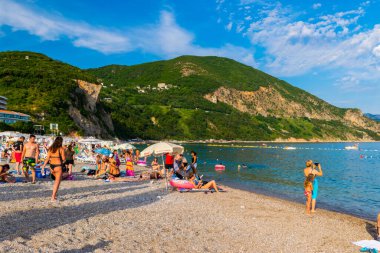 Jaz Beach, Karadağ - 4 Temmuz 2021: Güneşli şezlonglar ve şemsiyelerle kumlu kumsalda dinlenen insanlar. Budva Riviera. Yaz güneşli manzarası.