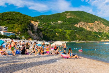 Jaz Beach, Karadağ - 4 Temmuz 2021: Güneşli şezlonglar ve şemsiyelerle kumlu kumsalda dinlenen insanlar. Budva Riviera. Yaz güneşli manzarası.