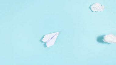 4k White paper airplane takes off, describing a circle and flies through the clouds, then lands. Blue background. Travel and transportation concept. Stop motion animation. Copy space.