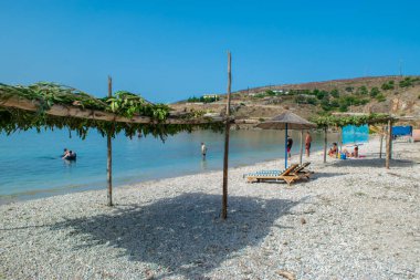 Qeparo plajı - 14 Temmuz 2021: güneşli yaz sabahında çakıl taşı plajında tatilciler. Arnavutluk. İyon Denizi. Yaz tatili ve rahatlama kavramı.