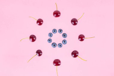 Berries of cherries and blueberries arranged in a circle. Pink background. Concept of berries season and proper nutrition. Flat lay. Copy space.