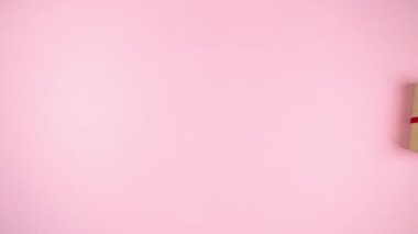 4k Holiday gift box wrapped in craft paper and tied with red ribbon dynamically moves. Copy space. Light pink background. Flat lay. Copy space. Stop motion animation.