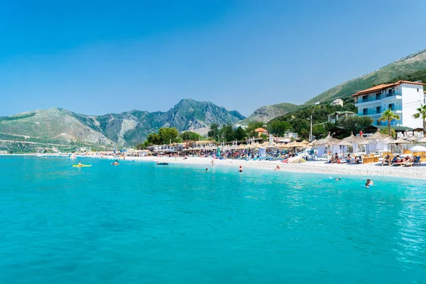 Borsh Beach, Albania - July 14, 202: Vacationers on pebble beach with clear blue water at foot of mountains.  Ionian Sea. Summer landscape. Concept of summer holidays and relaxation.