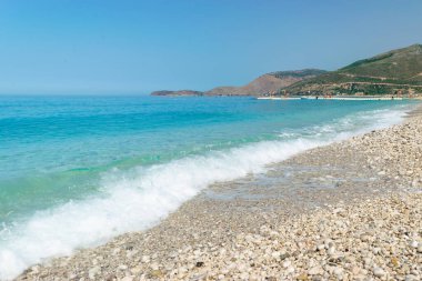 Pebble long Borsh beach with clear blue water. Cloudless sky. Albania. Ionian Sea. Summer landscape. Concept of summer holidays and relaxation.