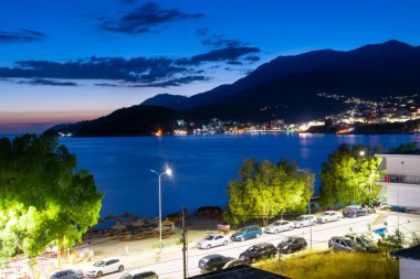 Twilight landscape of a resort Himare town located in a bay at the foot of the mountains. The village is beautifully lit by lanterns after sunset. Ionian sea. Albania.