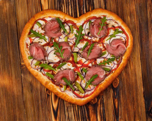 Restoran menüleri için ahşap arka planda kalp şeklinde pizza.