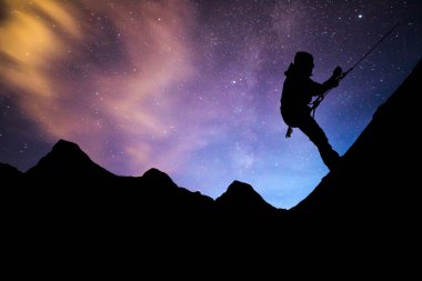 Gün batımında dağa tırmanan bir adamın silüeti. Adrenalin, güç, hırs. Gece vakti uzun süre manzara fotoğrafçılığı. Samanyolu Galaksisi, Birleşik Resim