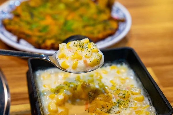 Kore usulü mısır, peynir ve mayonez, siyah bir tencerede, restoranda çekilmiş, kaşıkta tutulmuş.
