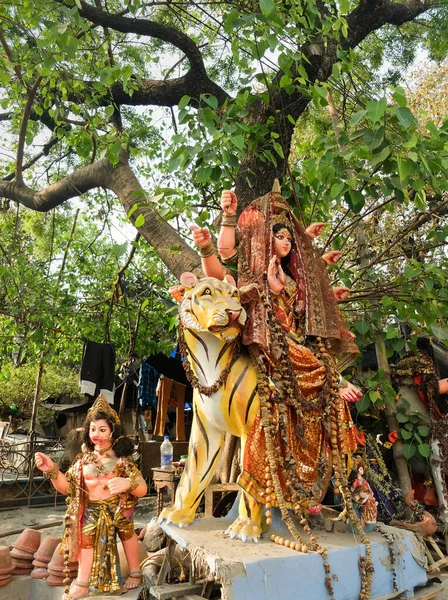 Next to the roadside in the city center,an Indian Godess sits astride a tiger with another female diety sitting below at the foot of the tree,all adorned with decorative garments and immitation jewellery.