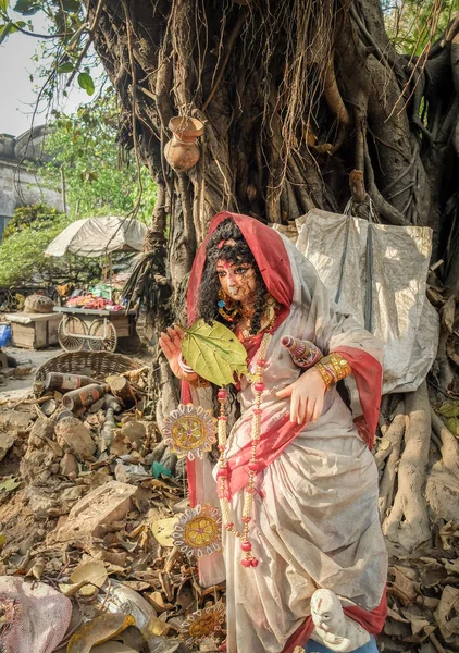 市内中心部の道路脇にある古い木の前には 廃れた女性神の姿がゴミの中に立っている — ストック写真