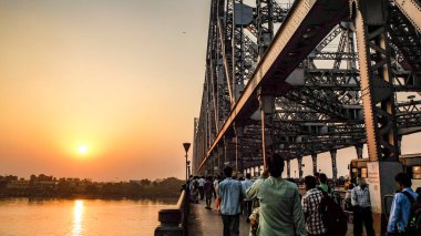Gün batımındaki Hooghly nehrinin karşısına bir sürü insan ve trafik köprüden karşıya geçerken..