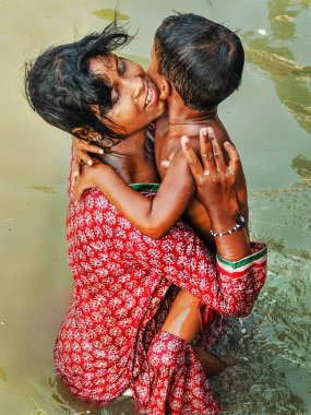 KOLKATA, Batı BENGAL / INDIA-MARCH 20 2018: Bir anne çocuğunu kucağında tutuyor Hooghly nehrinin kutsal sularında kendini ayinsel olarak suya batırıyor.